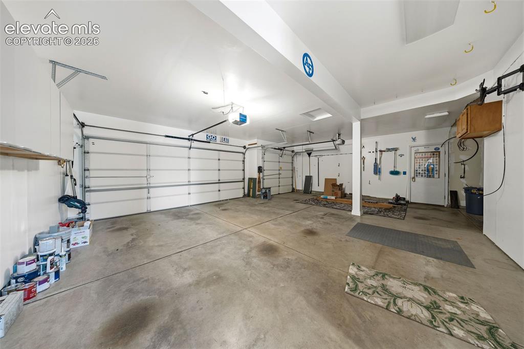 Image 21 of 50: Spacious garage with multiple overhead doors, concrete flooring, overhead l