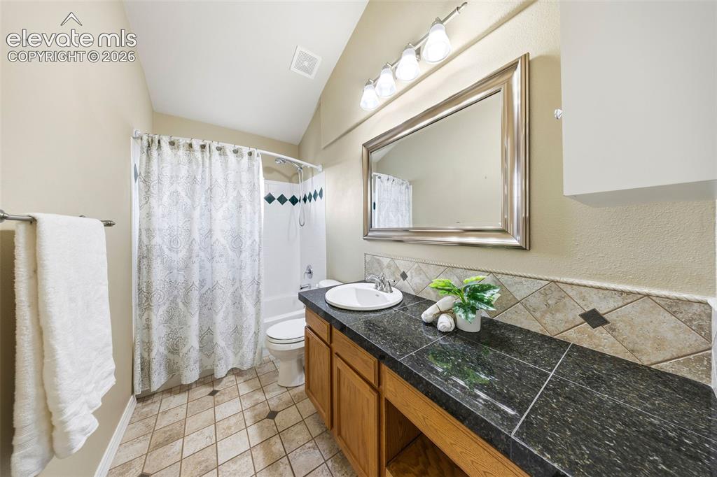 Image 30 of 50: Bathroom featuring a wood-finish vanity with a dark countertop, an integrat