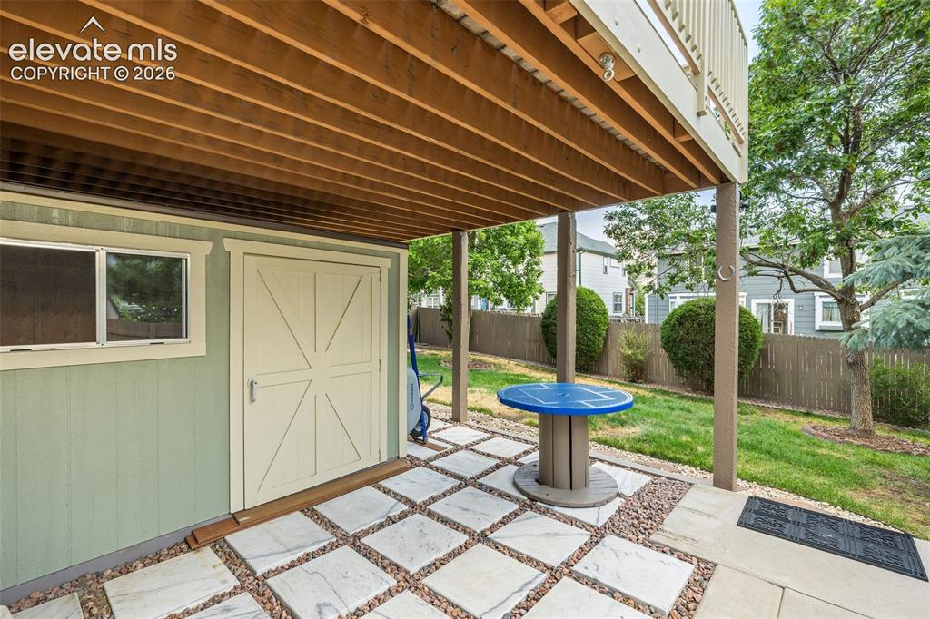 Image 43 of 50: Under-deck patio area featuring a light-colored paver and gravel surface