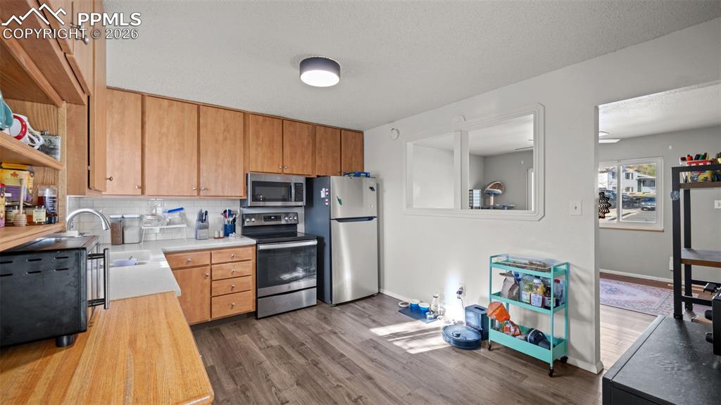 Image 6 of 22: Kitchen with stainless steel appliances, dark wood-style flooring, backspla