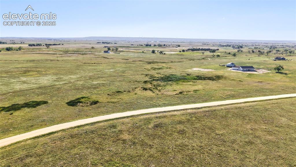 Image 2 of 9: Expansive open land featuring a winding dirt road and distant single-story 
