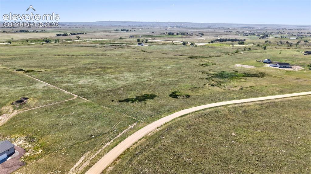 Image 5 of 9: Expansive grassland property featuring a gravel road, distant homes, scatte