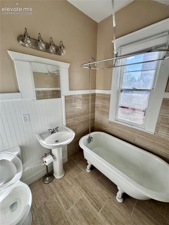 Image 11 of 48: Pedestal sink, clawfoot tub, window with blinds, tile flooring, and wall-mo