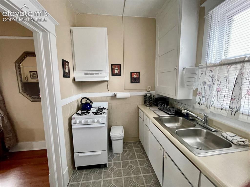 Image 32 of 48: White cabinetry, dual basin stainless steel sink, gas range, and patterned