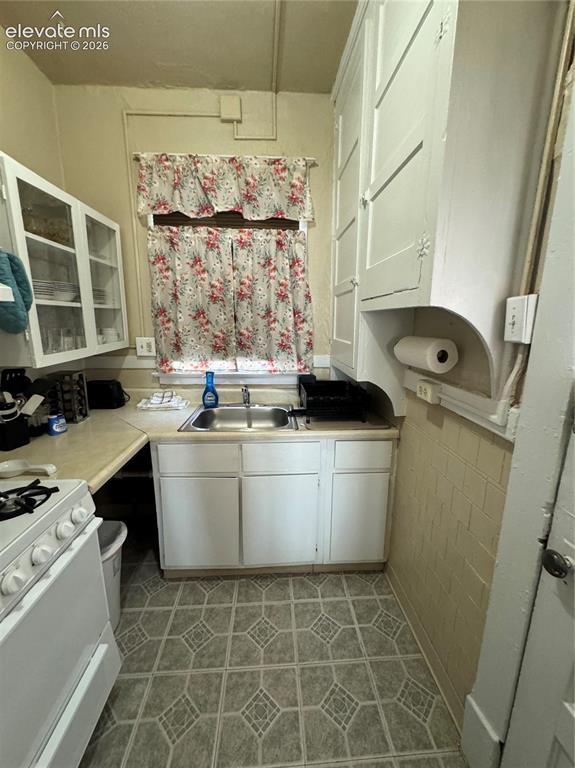 Image 37 of 48: Compact kitchen featuring a stainless steel sink, white cabinetry, and patt