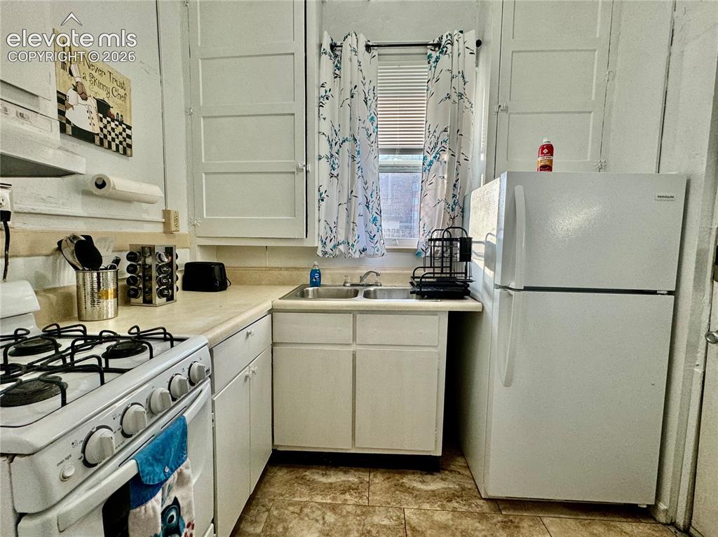 Image 6 of 50: Kitchen featuring white cabinetry, a dual-basin sink, a white gas range, an
