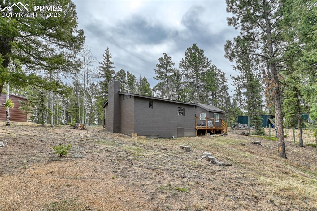 Image 29 of 48: Back of house with a chimney, a wooden deck, and concrete block siding