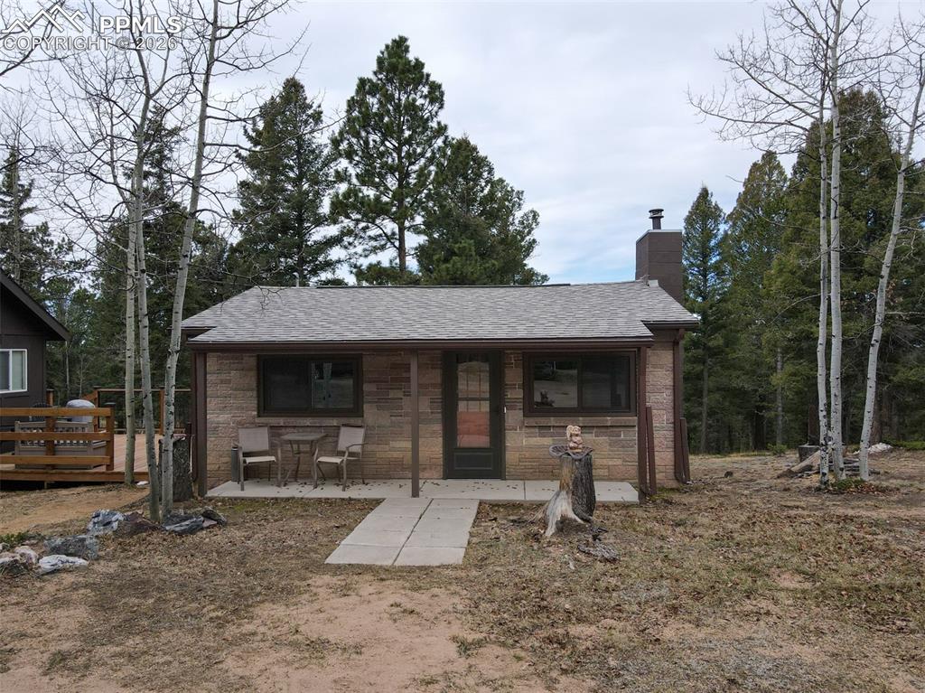 Image 32 of 48: View of front facade featuring a chimney, roof with shingles, and stone sid