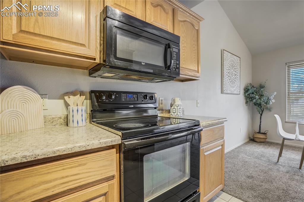 Image 10 of 42: Kitchen featuring black appliances, light carpet, light stone counters, and