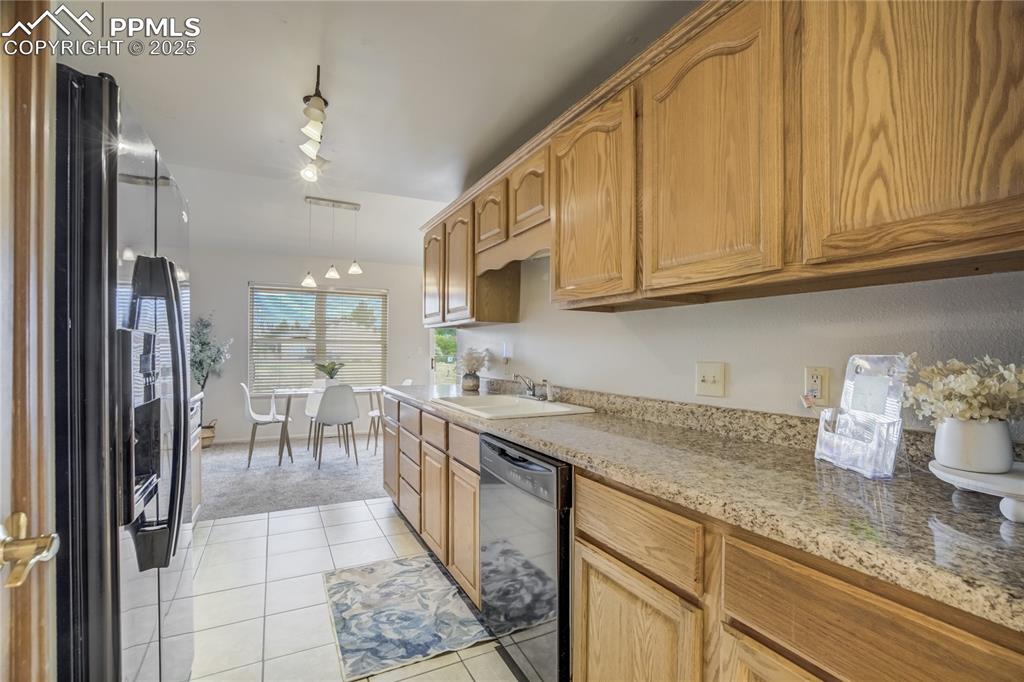 Image 11 of 42: Kitchen with black dishwasher, freestanding refrigerator, light tile patter