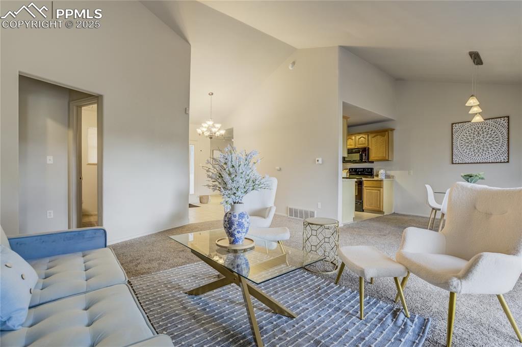Image 6 of 42: Living area featuring light colored carpet, a chandelier, and high vaulted 