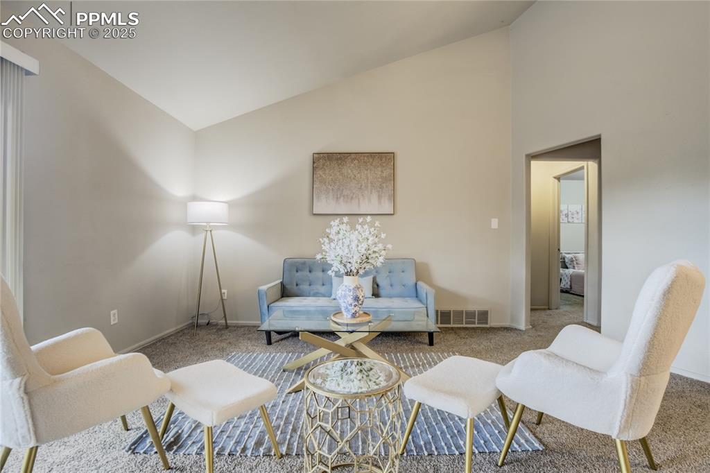Image 7 of 42: Living area with high vaulted ceiling and carpet