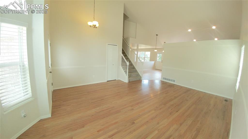 Image 5 of 39: Spare room with high vaulted ceiling, stairs, a chandelier, and light wood