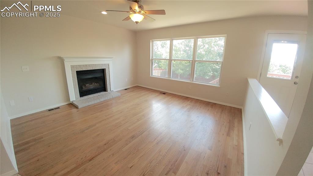 Image 9 of 39: Unfurnished living room with light wood finished floors, a brick fireplace,