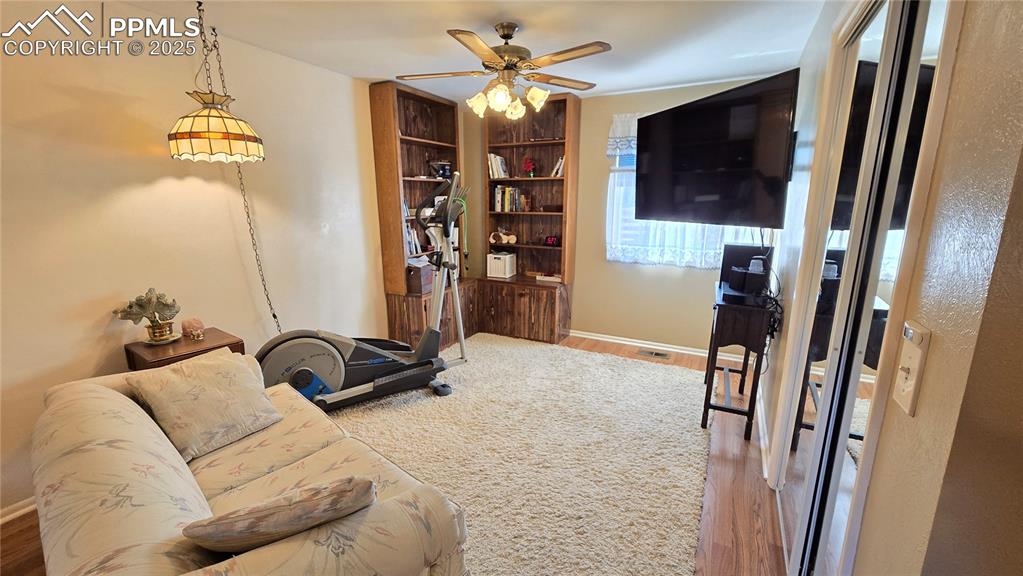 Image 12 of 42: Living room featuring light wood-style flooring, ceiling fan, and built in 