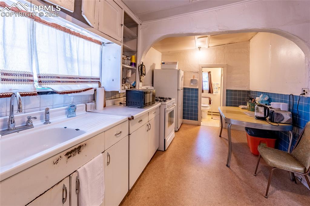 Image 7 of 21: Kitchen featuring light countertops, white gas stove, open shelves, tile wa