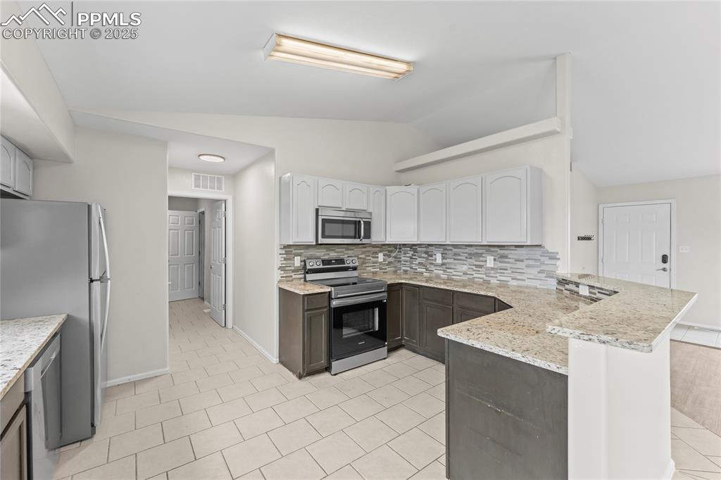 Image 6 of 29: Kitchen featuring a peninsula, stainless steel appliances, decorative backs