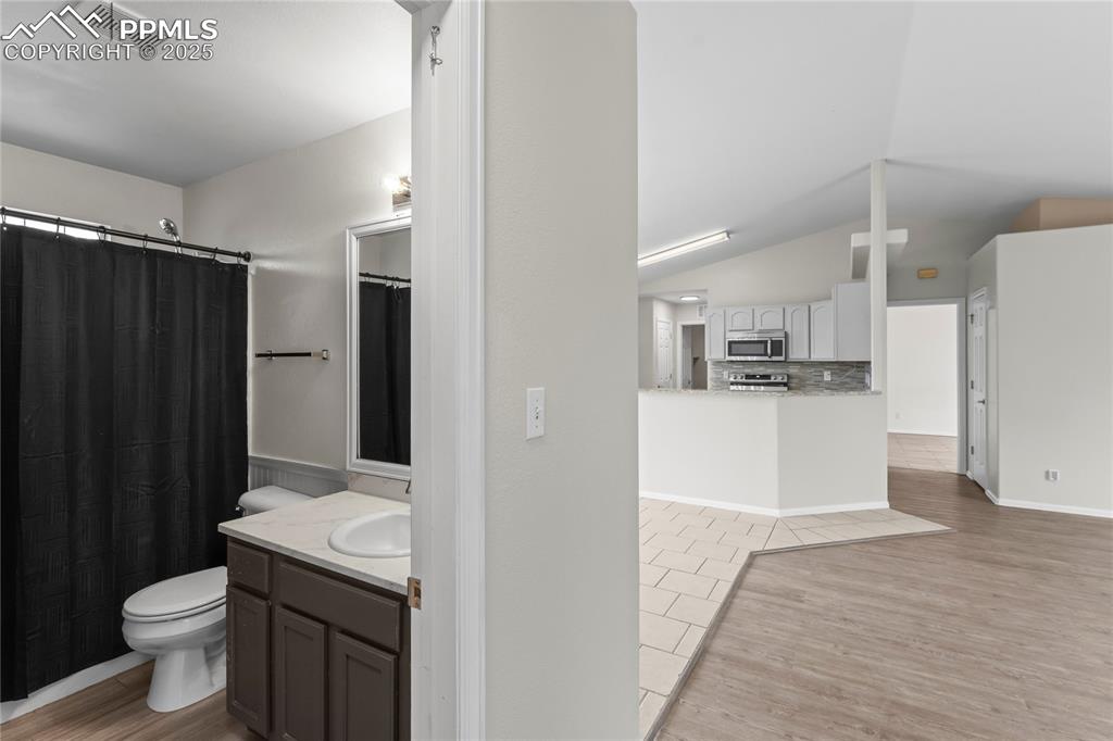 Image 9 of 29: Bathroom with wood finished floors, decorative backsplash, vanity, vaulted 