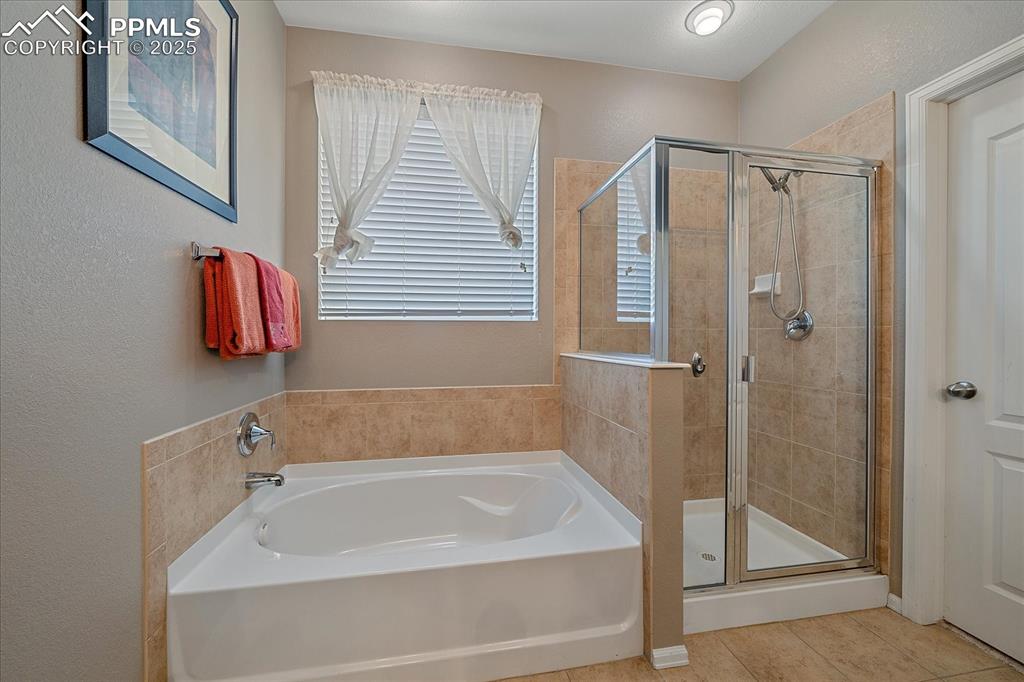 Image 21 of 49: Full bath featuring a stall shower, a bath, a textured wall, and tile patte
