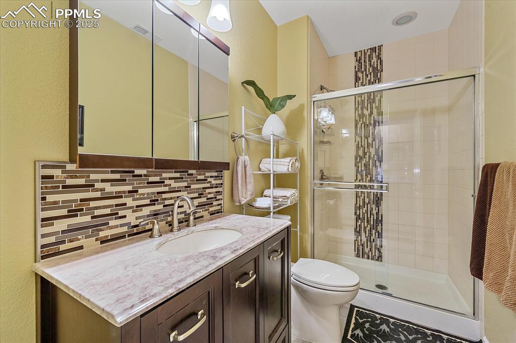 Image 35 of 49: Bathroom in basement with vanity, a shower stall, and decorative backsplash