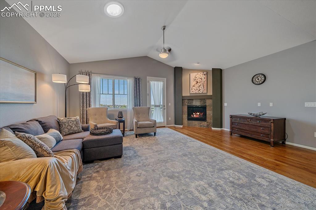 Image 8 of 49: Living room with wood finished floors, a tiled fireplace, and vaulted ceili