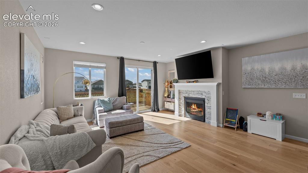 Image 16 of 46: Wood-finish flooring, recessed lighting, and a fireplace with a stone surro