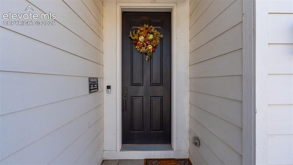 Image 4 of 46: White horizontal siding, black paneled entry door, digital doorbell