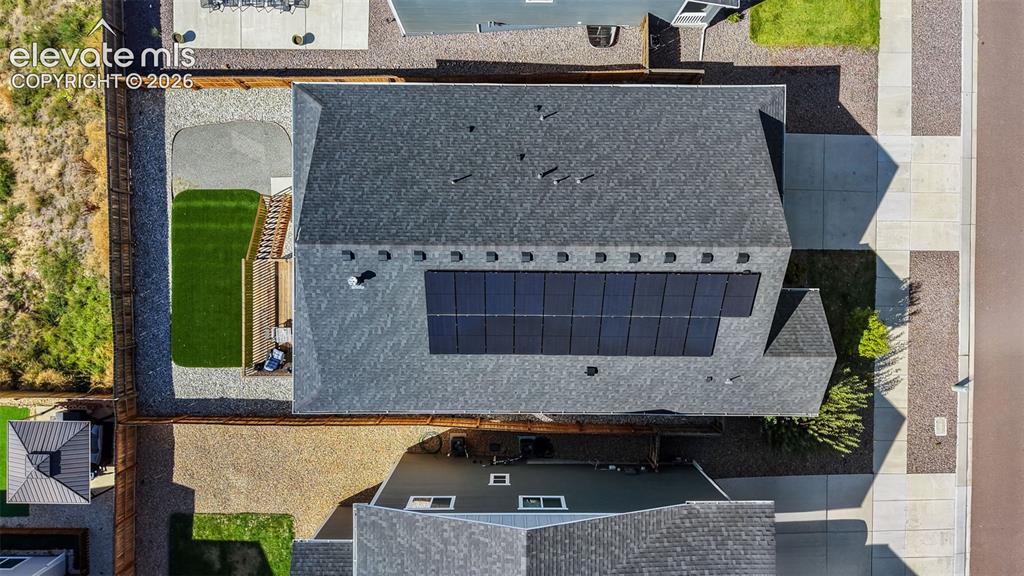 Image 41 of 46: Shingled roof with integrated solar panels, fenced yard, gravel landscaping