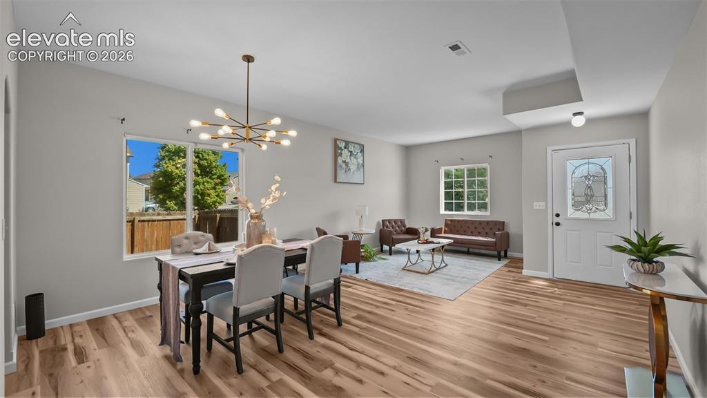 Image 6 of 47: Open-concept living space with wood-finish flooring, a contemporary chandel