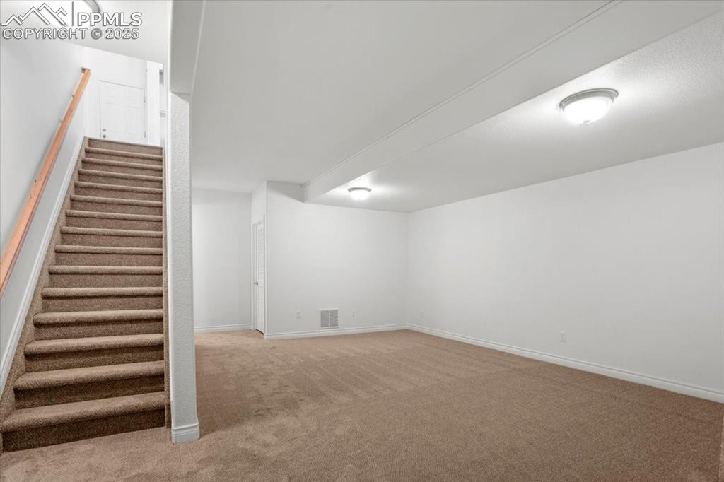 Image 18 of 31: Finished basement with stairs and light colored carpet