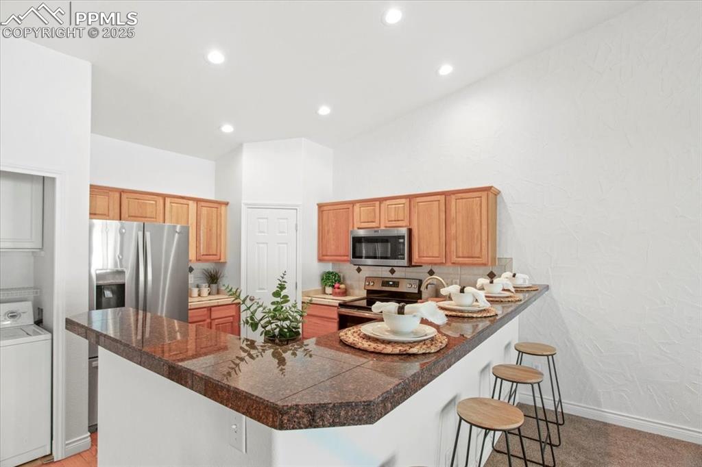 Image 4 of 31: Kitchen with a kitchen bar, a peninsula, washer / clothes dryer, stainless