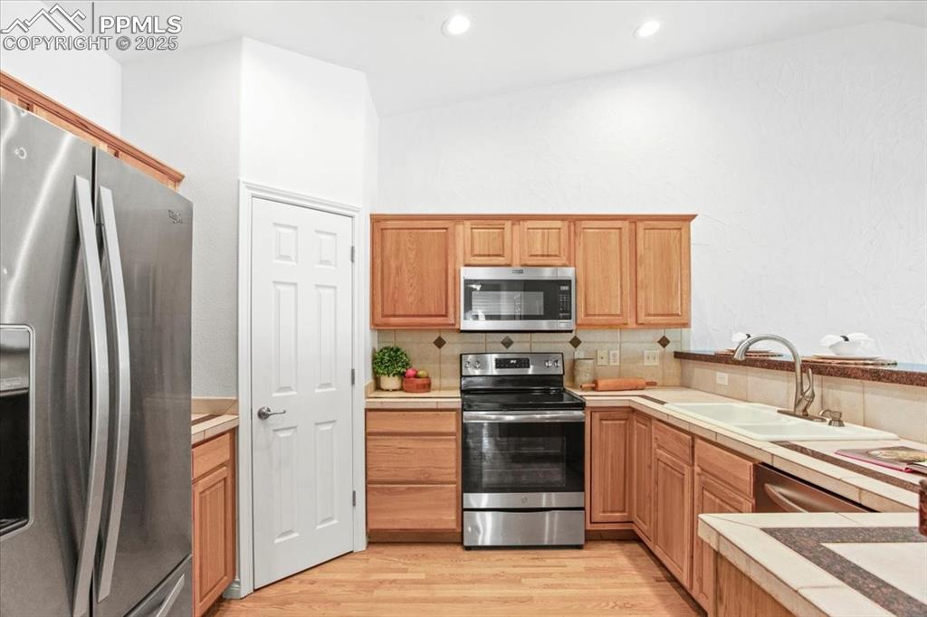 Image 6 of 31: Kitchen with stainless steel appliances, backsplash, light wood-type floori