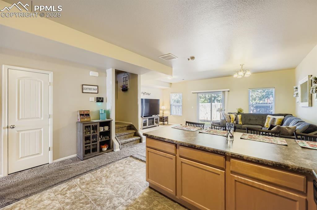 Image 10 of 27: Kitchen with open floor plan, dark countertops, a chandelier, light brown c