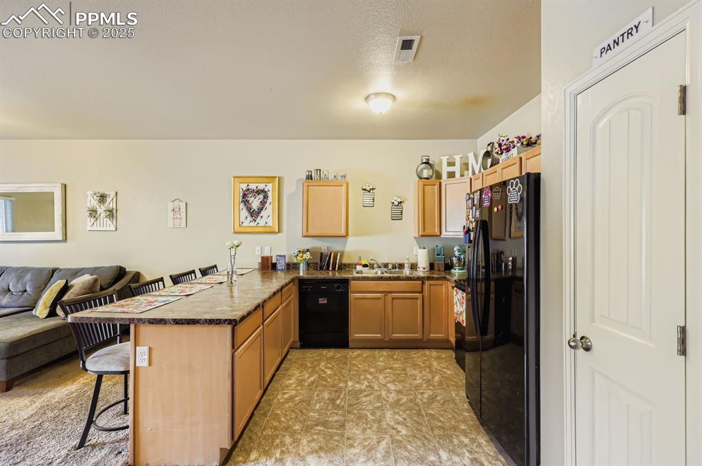 Image 11 of 27: Kitchen with a kitchen bar, open floor plan, a peninsula, black appliances,