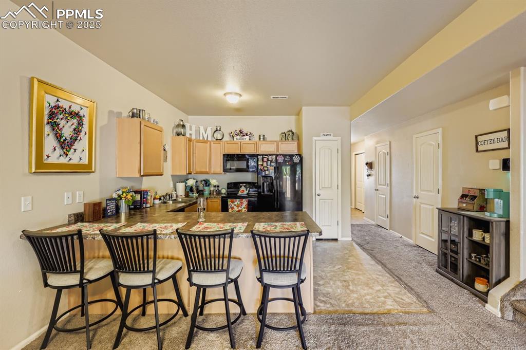 Image 12 of 27: Kitchen with black appliances, a kitchen bar, light brown cabinets, a penin