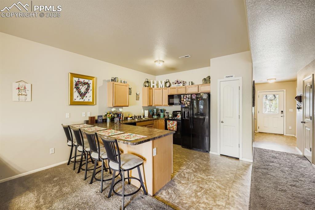 Image 8 of 27: Kitchen featuring dark countertops, black appliances, a peninsula, a breakf
