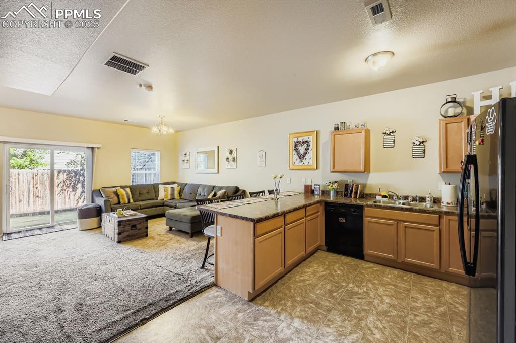 Image 9 of 27: Kitchen with a peninsula, black appliances, a kitchen bar, a textured ceili