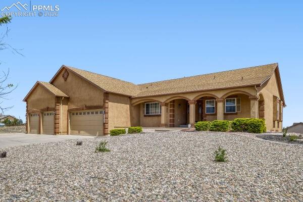 Image 1 of 31: Stucco exterior with arched entry porch, a multi-car garage, and a gravel f