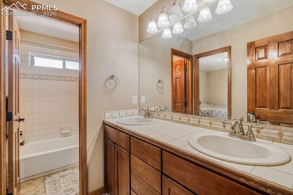 Image 20 of 31: Bathroom featuring a dual vanity with tile countertop, wood cabinetry, and
