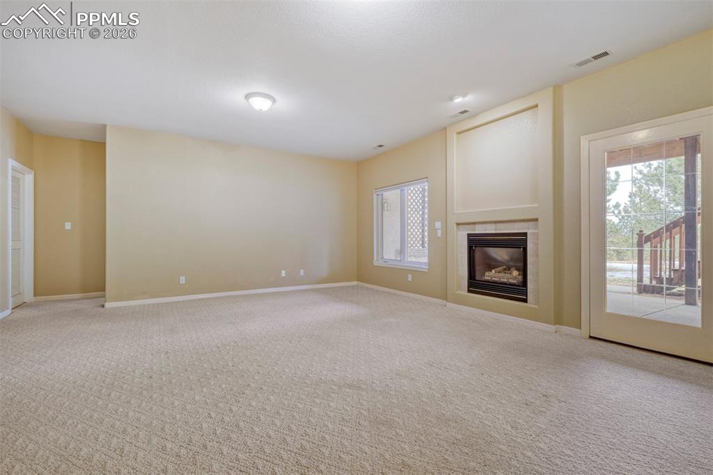 Image 25 of 50: Family room with a tile fireplace and carpet flooring and walkout to covere