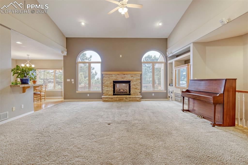 Image 9 of 50: living room with a stone fireplace, carpet flooring, ceiling fan, and hangi