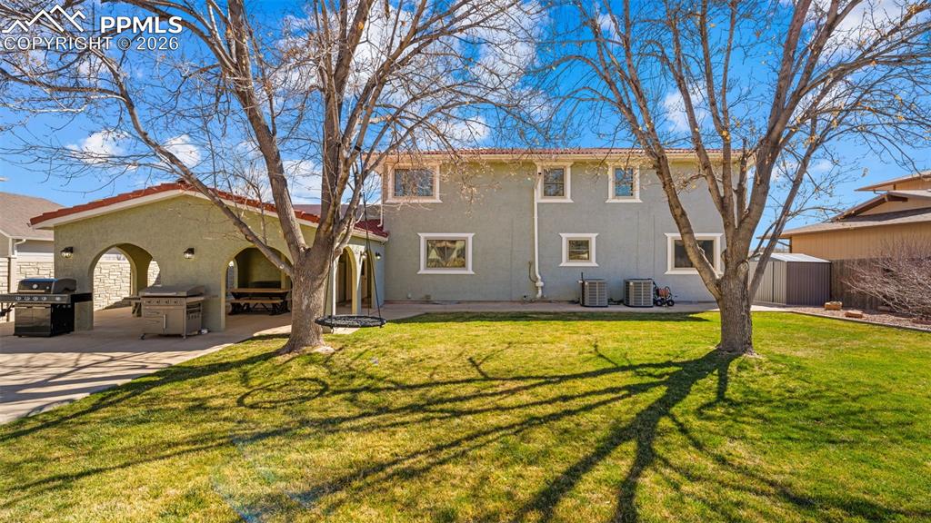 Image 27 of 44: Back of house with a yard, a shed, stucco siding, and a patio area
