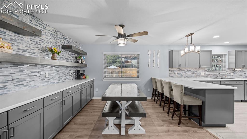 Image 5 of 44: Kitchen featuring gray cabinetry, backsplash, a peninsula, a breakfast bar,