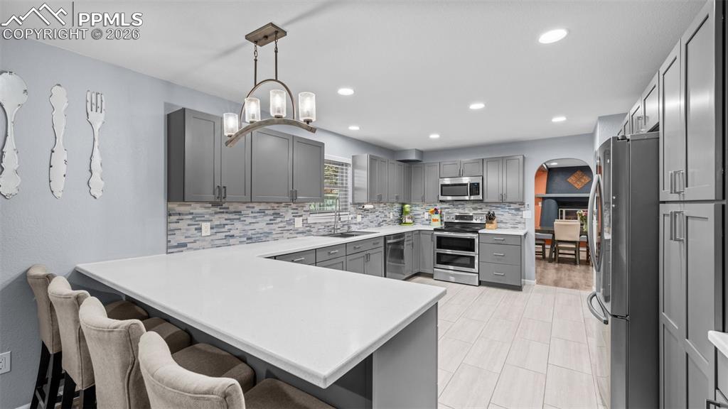 Image 9 of 44: Kitchen with gray cabinetry, stainless steel appliances, a peninsula, arche