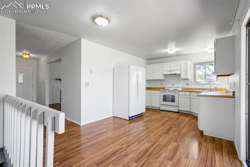 Image 13 of 50: The kitchen features wood-toned flooring, white cabinetry, and white applia