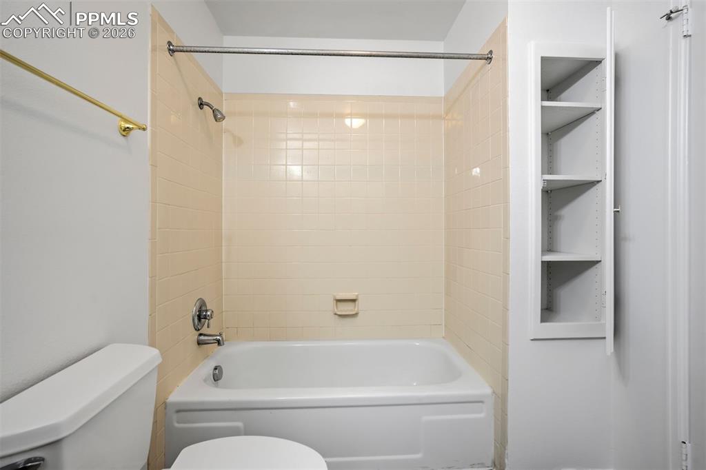 Image 23 of 50: The bathroom features a white bathtub with a shower, surrounded by tiled wa
