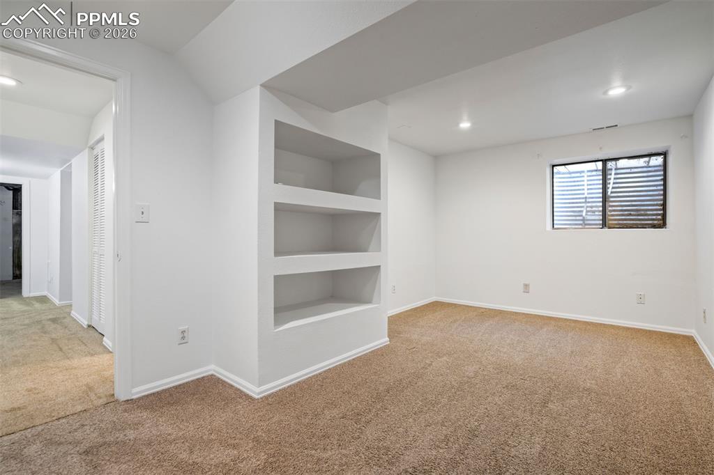 Image 38 of 50: This room features light brown carpeting, built-in shelving, and recessed l