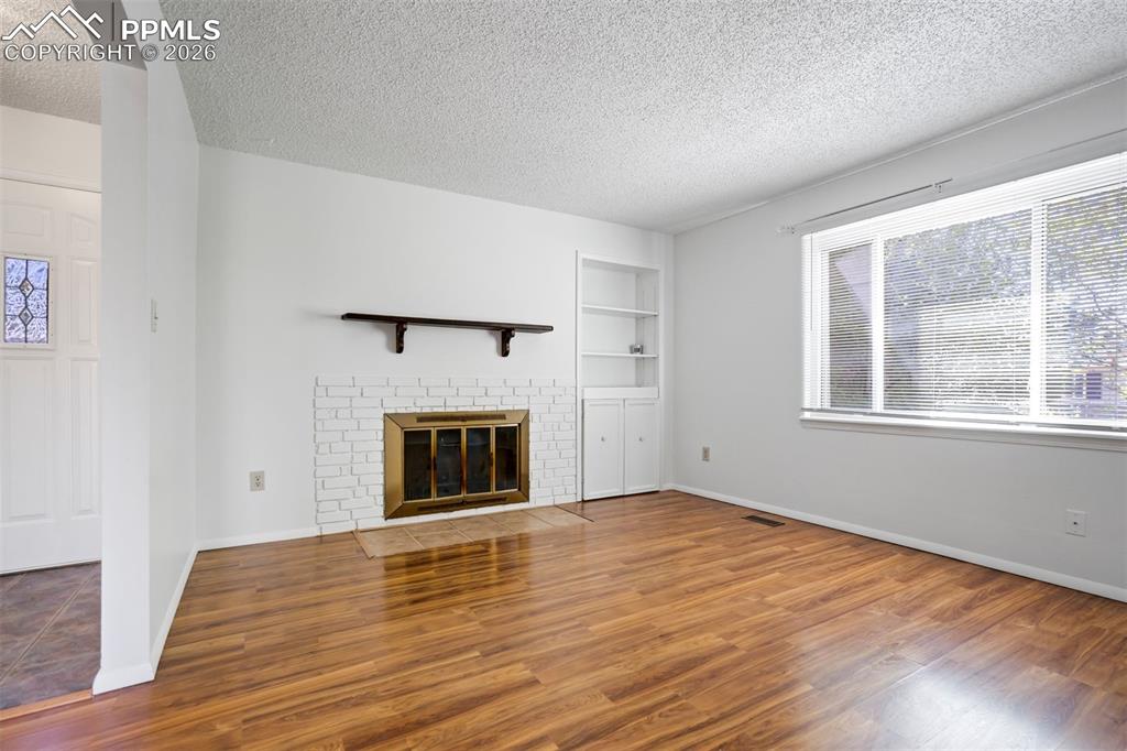 Image 4 of 50: Living room featuring hardwood flooring, a white brick fireplace with a bra