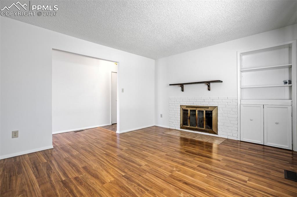 Image 6 of 50: Living area featuring hardwood flooring, a white brick fireplace with a bra