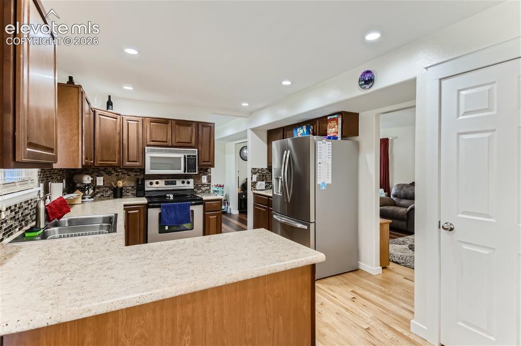 Image 12 of 49: Kitchen featuring wood-finish cabinetry, stainless steel appliances, mosaic